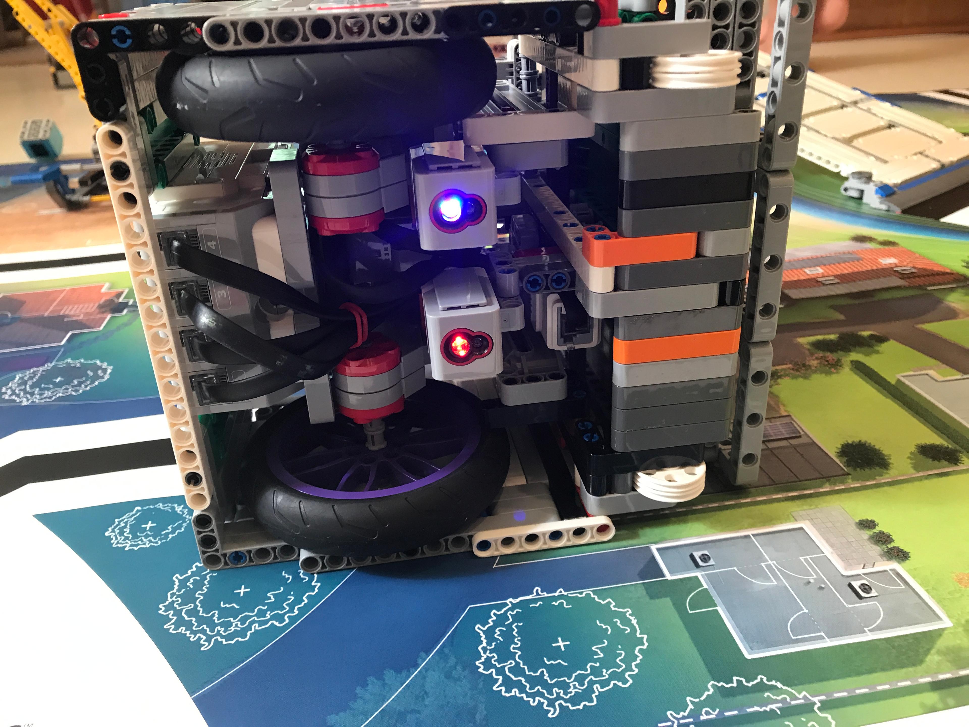 Fig. 3 · The forward reflected-light sensors (lit blue and red) read the printed field lines the robot follows between mission sites.